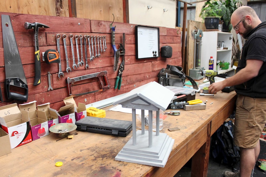 A man works on a bench surrounded by tools.