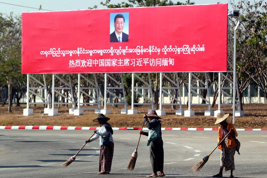 Municipal workers sweep on a road near a welcoming billboard for Chinese President Xi Jinping.