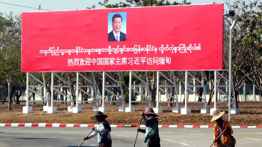 Municipal workers sweep on a road near a welcoming billboard for Chinese President Xi Jinping.