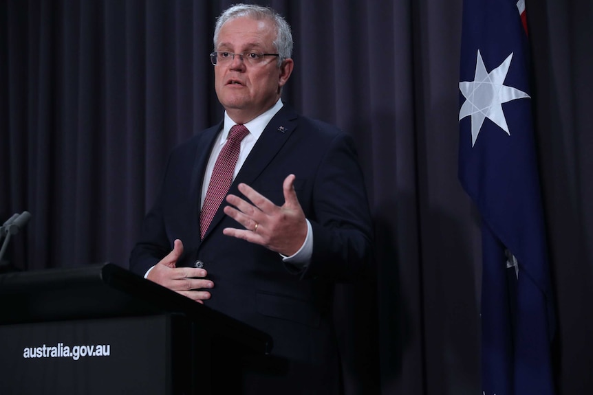 Scott Morrison gestures with his hands while speaking at press conference in front of an Australian flag.