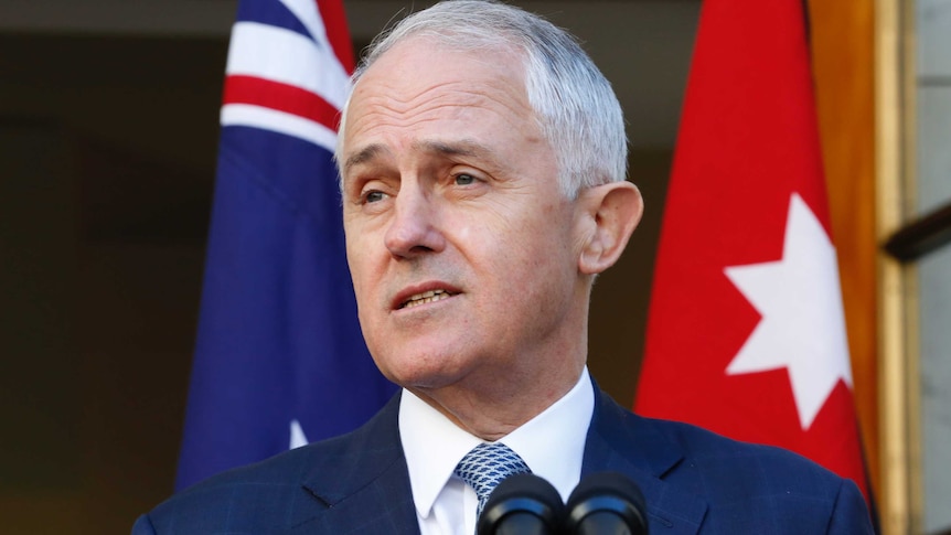 Prime Minister Malcolm Turnbull stands in front of the Australian and Jordanian flags at a press conference
