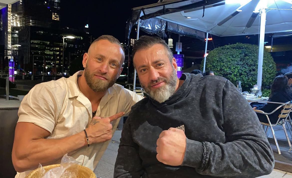 Two men leaning toward each other, giving a thumbs up.