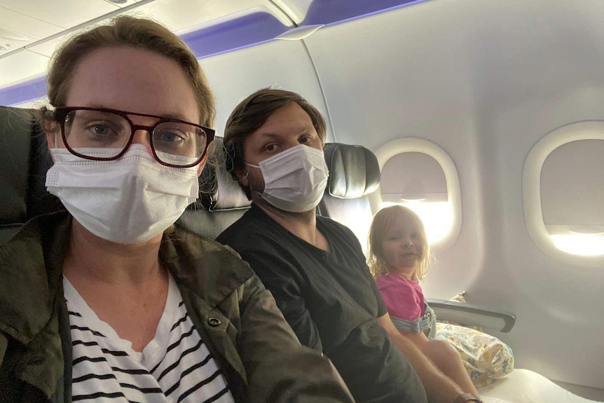 A woman and man wear masks on a plane. A toddler sits beside them.