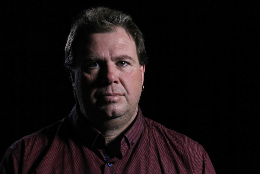 Andrew Hack stares at the camera with a black background.