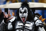 Gene Simmons, wearing black and white makeup and a silver costume, sticks his tongue out and makes rock and roll hand signs