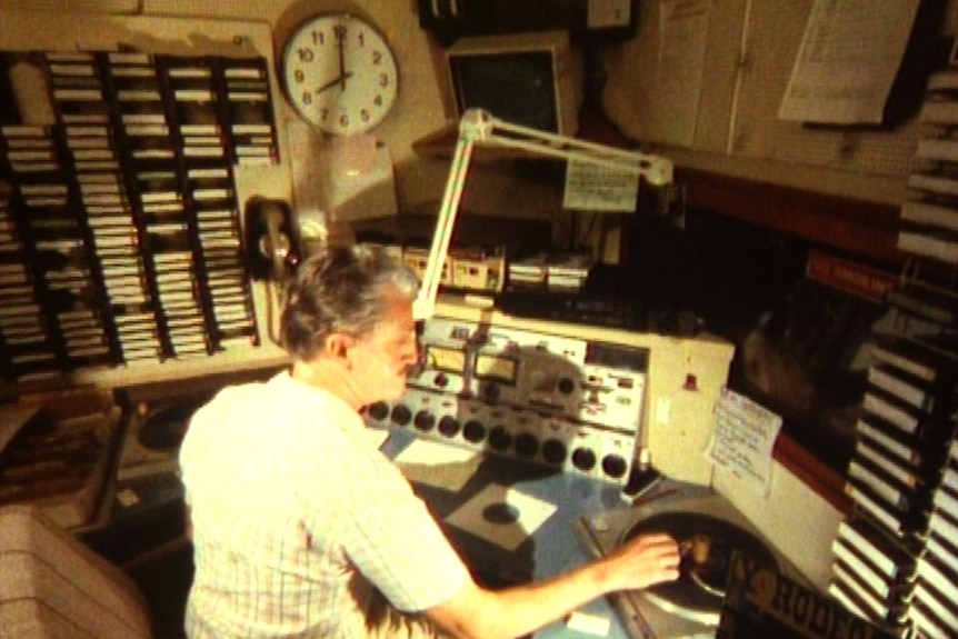 A man sits in a radio studio with microphone and record player