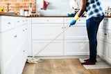 A person uses a mop in the kitchen, in an image depicting household labour.