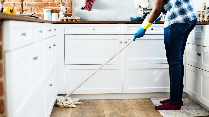 A person uses a mop in the kitchen, in an image depicting household labour.