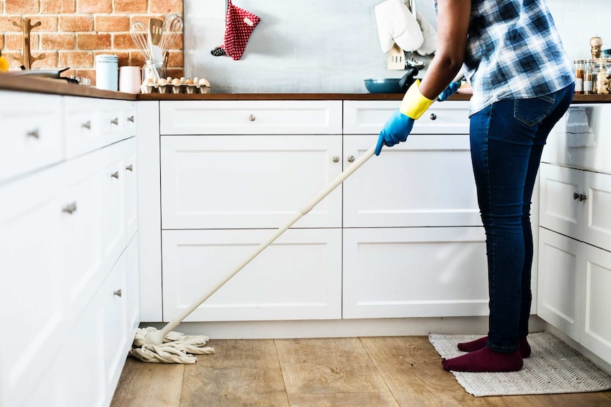 A person uses a mop in the kitchen to depict how to avoid fights about cleaning and mess for a happier household.
