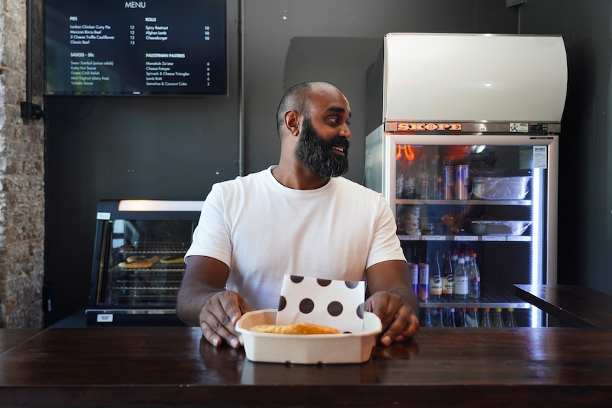 a man with a beard stands behind a bakery counter