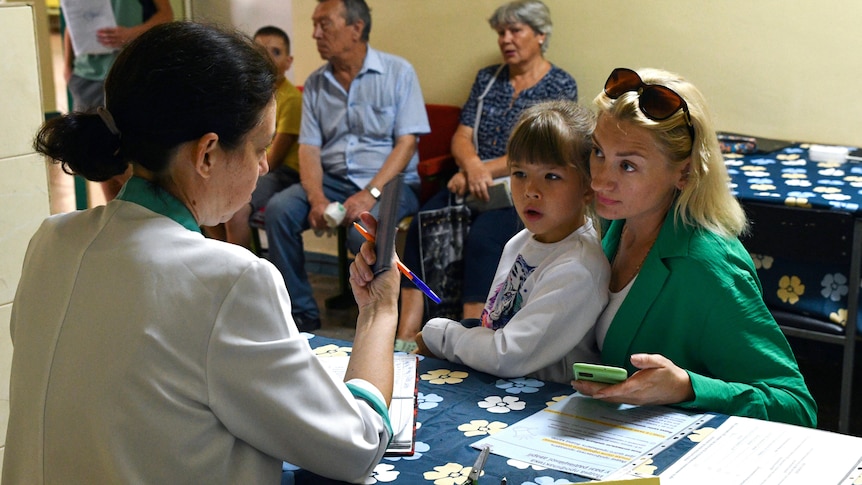 一名妇女和儿童在碘片分发点的办公桌前与医务人员交谈