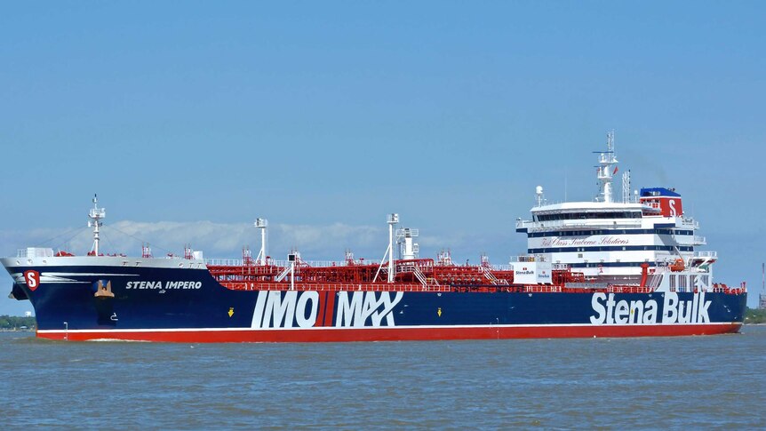 On a bright clear day, the British oil tanker Stena Impero clad in red white and blue colours sits in clear blue waters.