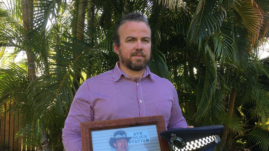Son od missing police officer Senior Sergeant Mick Isles, Steven Isles, holds a photo of his father and a police hat.