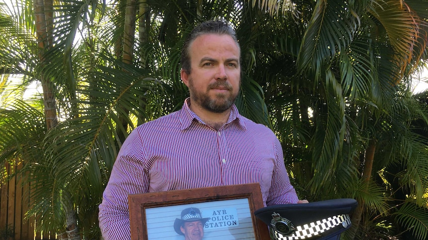 Son od missing police officer Senior Sergeant Mick Isles, Steven Isles, holds a photo of his father and a police hat.