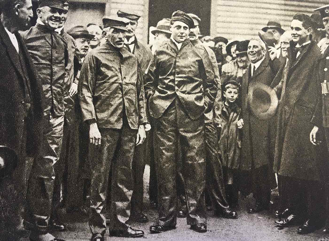 O primeiro-ministro e o príncipe estão no meio da multidão vestindo macacão e boné.