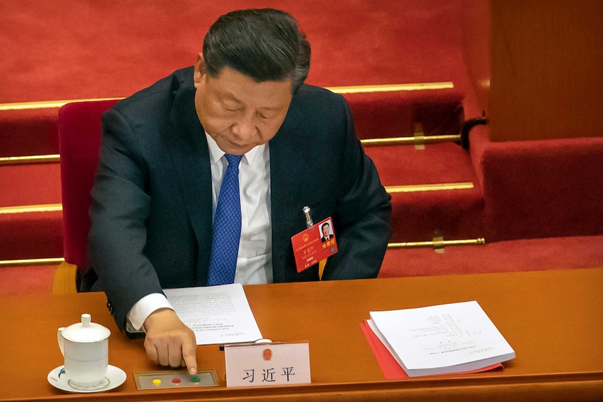 Chinese President Xi Jinping reaches to vote by pressing a row of buttons on a panel.