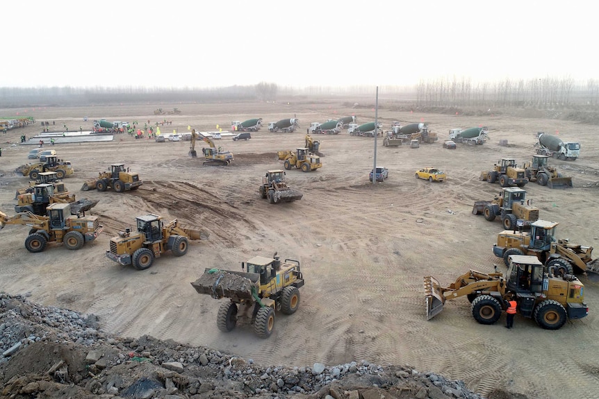 Dozens of tractors and cement trucks on a flat dusty ground.