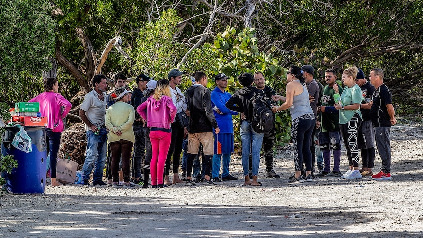 A group of people stand in a circle listening to one of the group talk