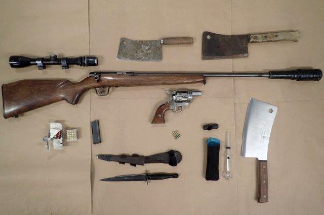 Display of weapons on brown paper, inlcuidng, rifle, silencer, 3 meat cleavers, daggers, handgun and ammunition.