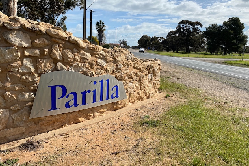 A stone wall with a sign that says Parilla on it, a road in the background.