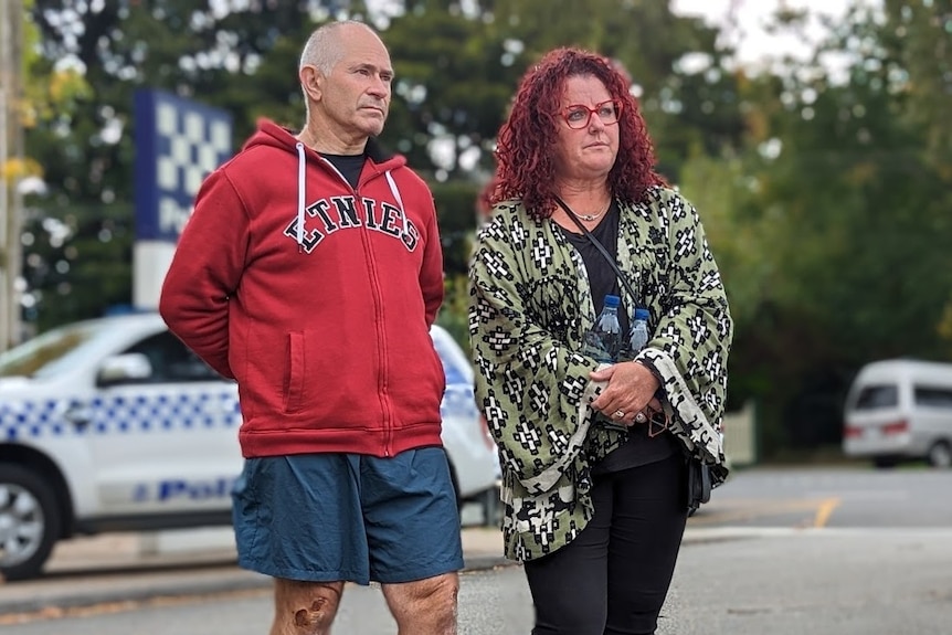 Robert Clarke, wearing a red hoodie and shorts which show his injured leg, with his wife Donna.