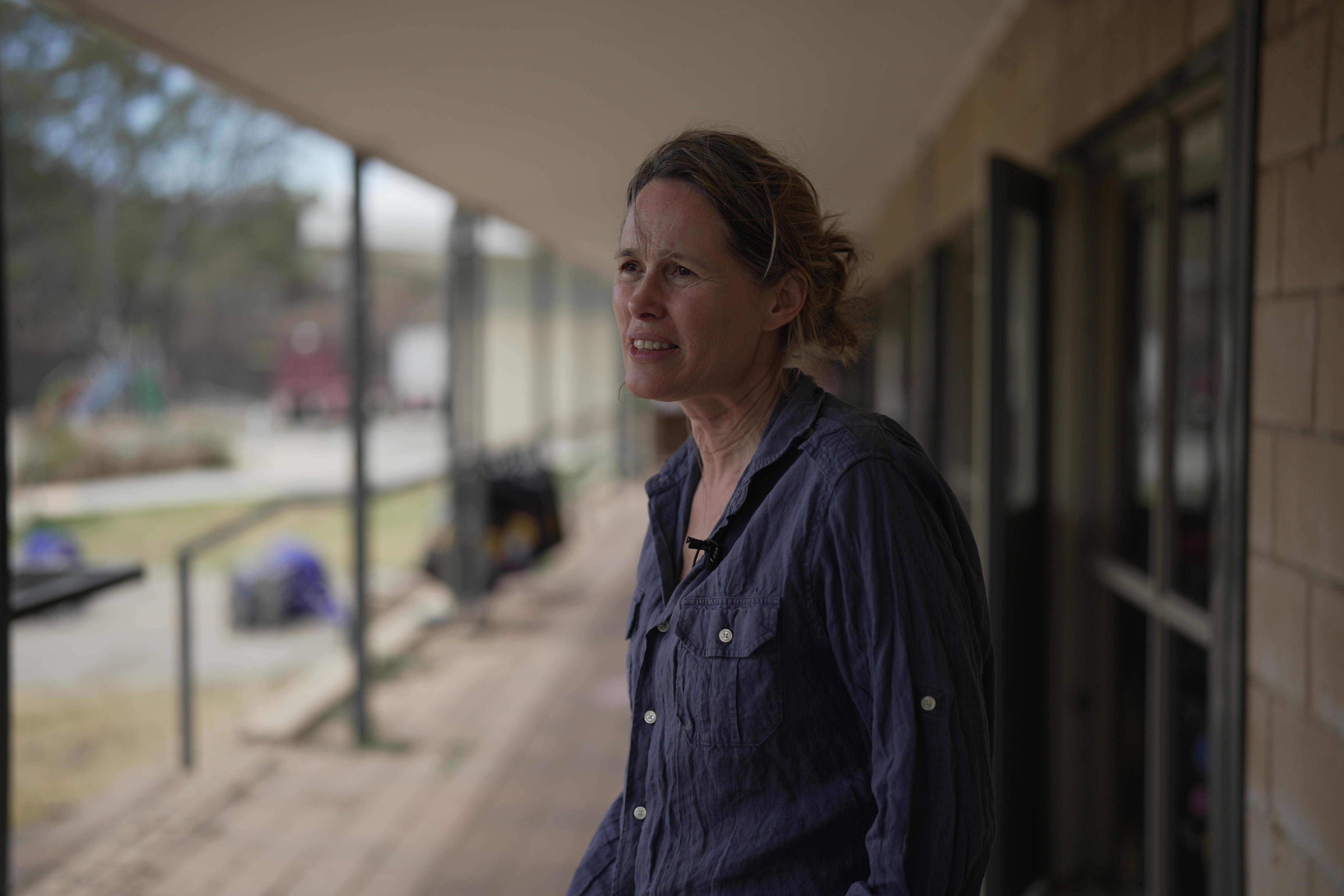 Uma mulher com uma camisa azul parada sob o toldo de um prédio olhando para o lado da moldura