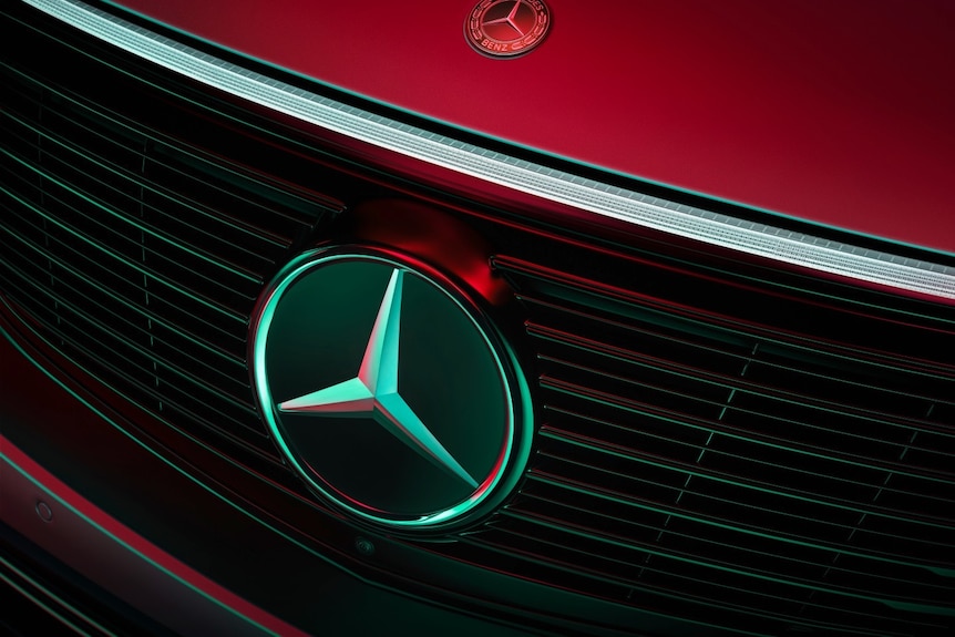 The badge on the front of a red Mercedes-Benz car.