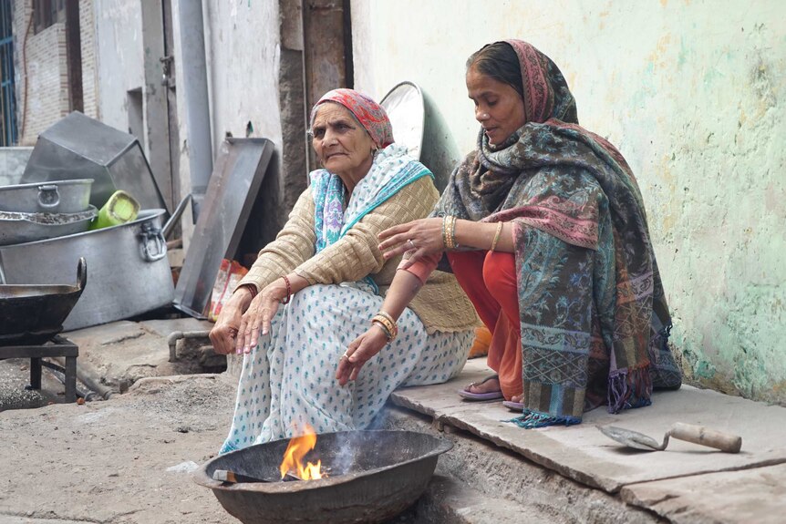 Two women sit around a fire on the side of a road in Delhi.