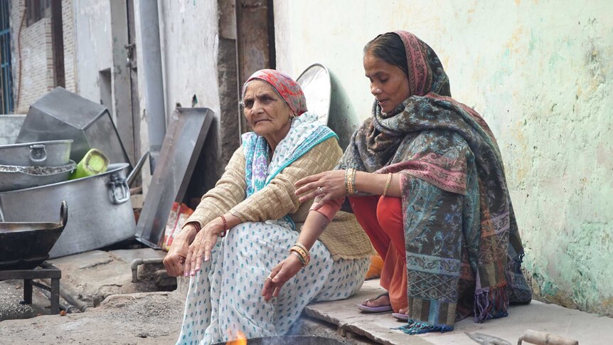 Two women sit around a fire on the side of a road in Delhi.