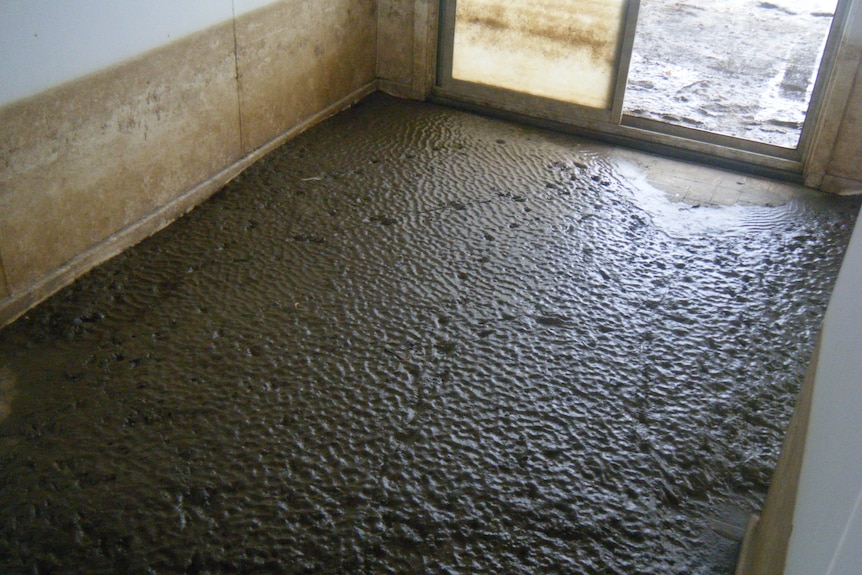 A sodden and muddy floor, with water marks on the wall of the shack.