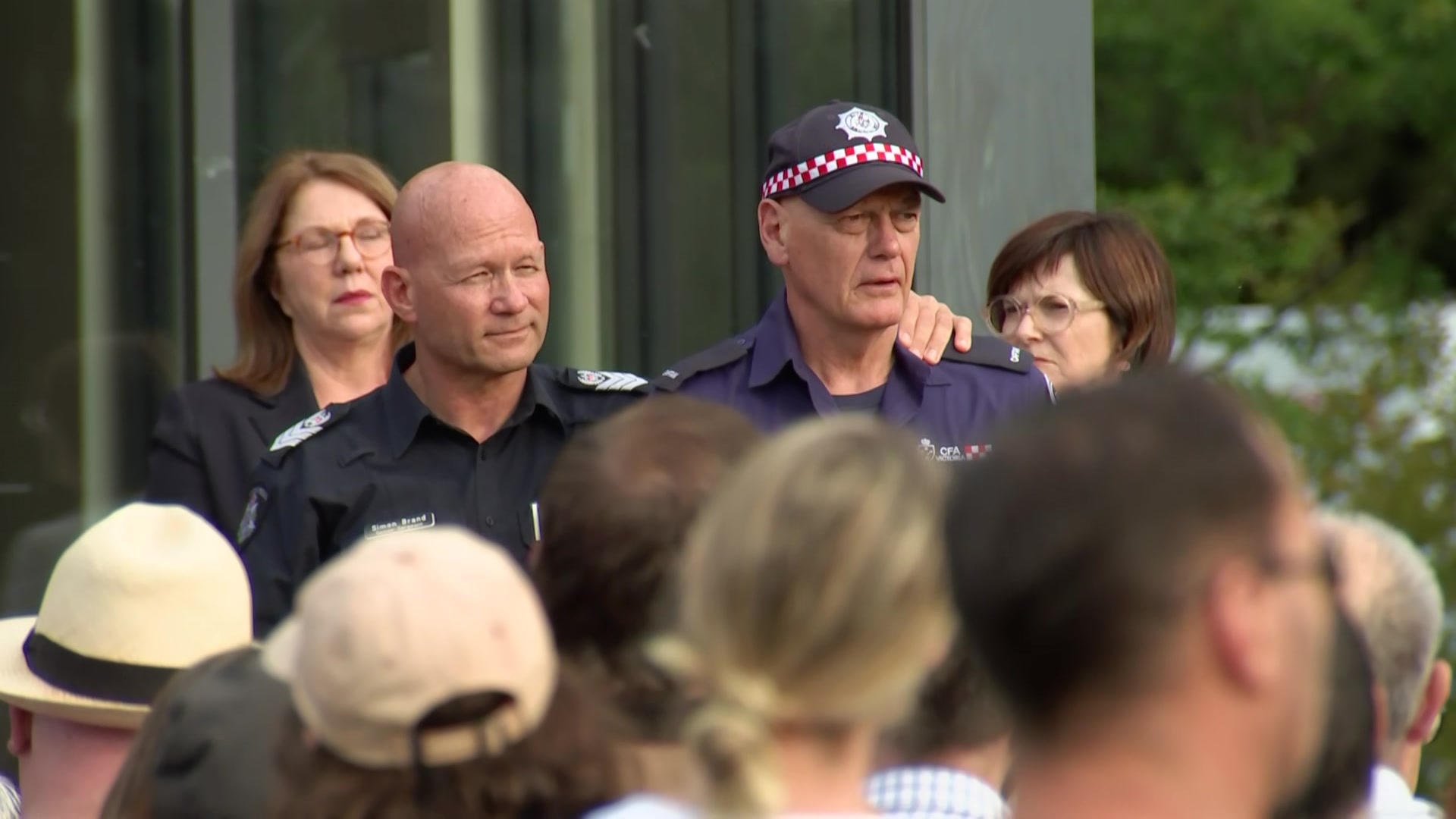 A Victoria Police officers with his arm around a CFA member standing in front of a large crowd.
