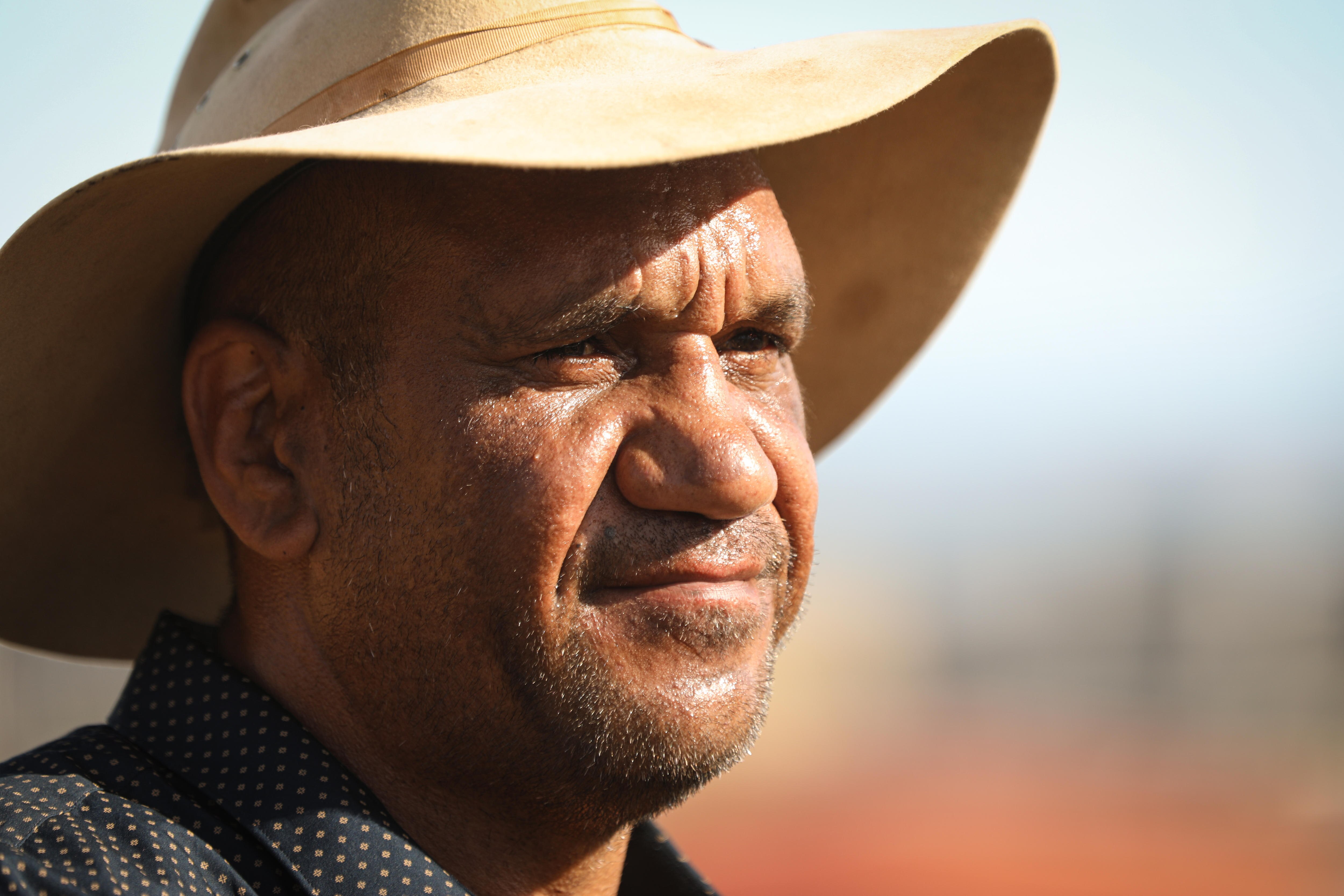 A man wearing an akubra looks away from the camera with a  neutral facial expression.