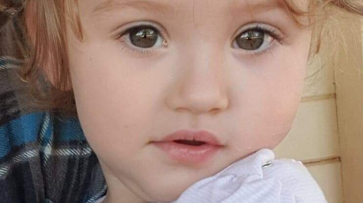 A young mother hold her infant daughter who looks into the camera.