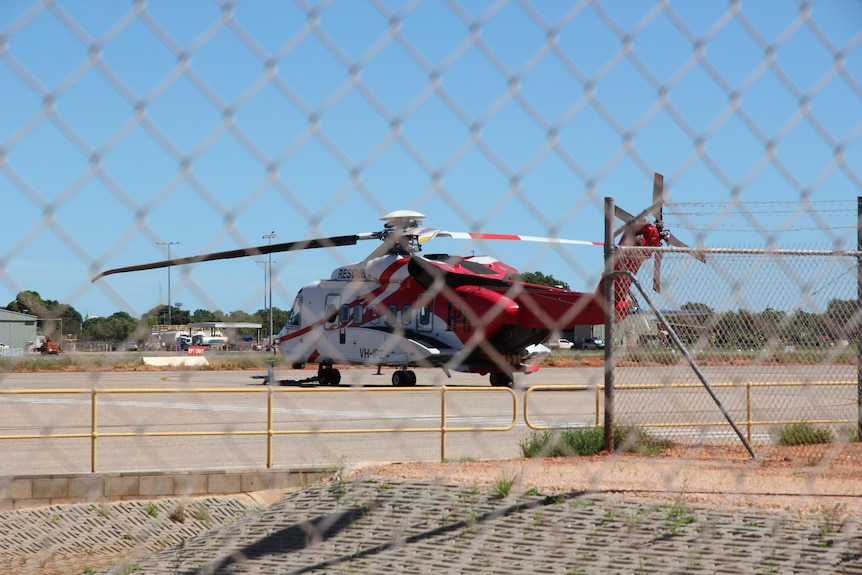 A red and white helicopter seen through a fence