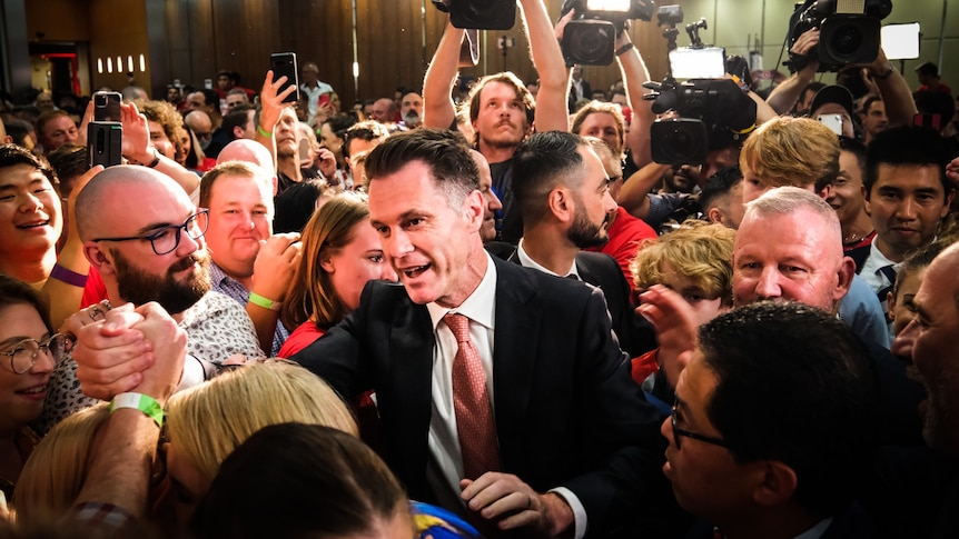 a man surrounded by people celebrating in a room after an election result