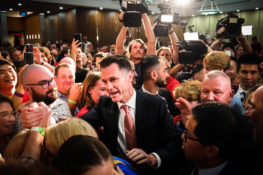 a man surrounded by people celebrating in a room after an election result