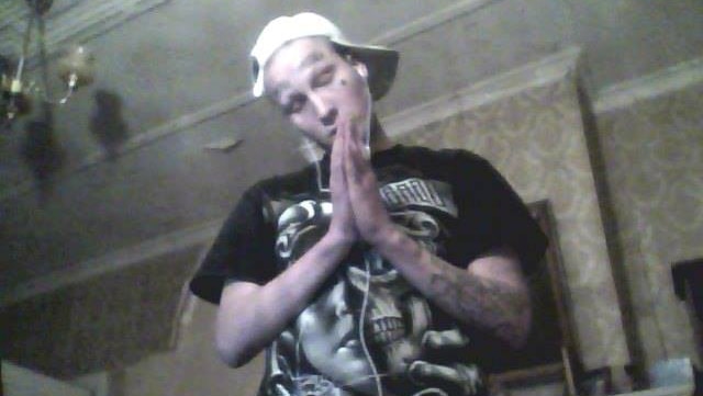 A man with a white cap, tattoos and black t-shirt praying inside