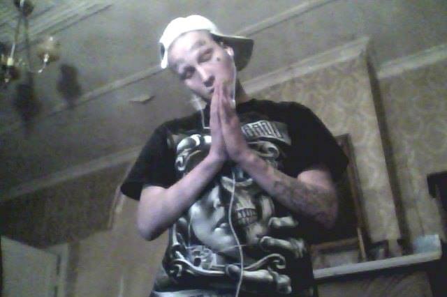 A man with a white cap, tattoos and black t-shirt praying inside