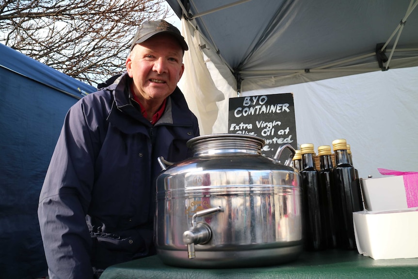 a stainless steel decanter next to bottles of olive oil