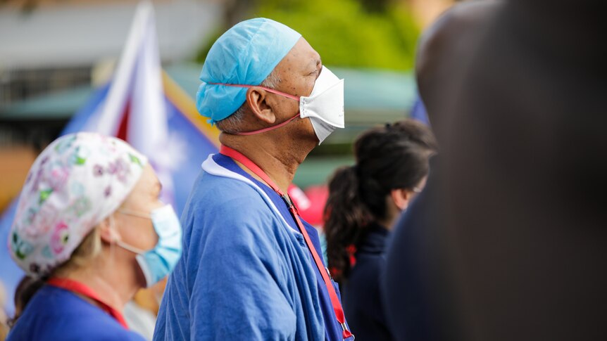 Health workers in uniform and masks gather in crowds outside a hospital.