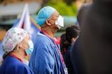 Health workers in uniform and masks gather in crowds outside a hospital.