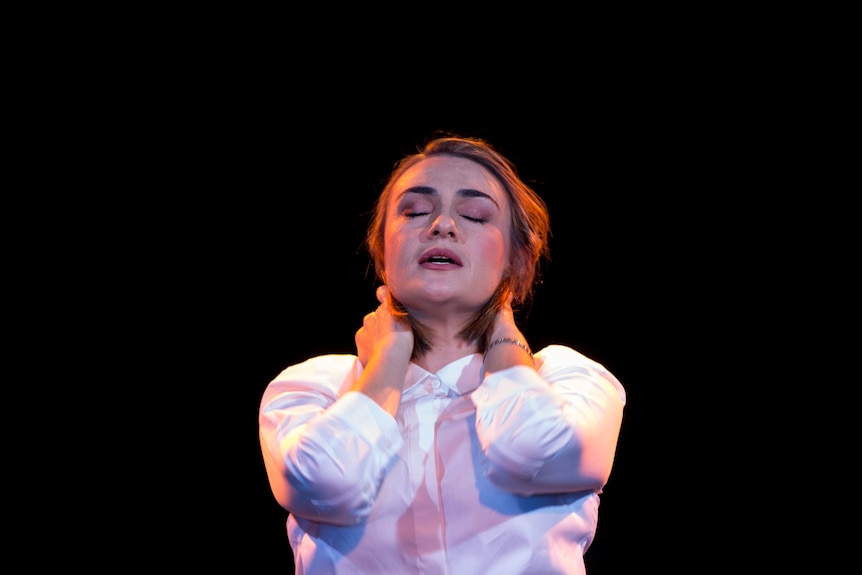 A 30-something woman with cropped hair and a white button-down looks relieved, her eyes closed and hands massaging her neck