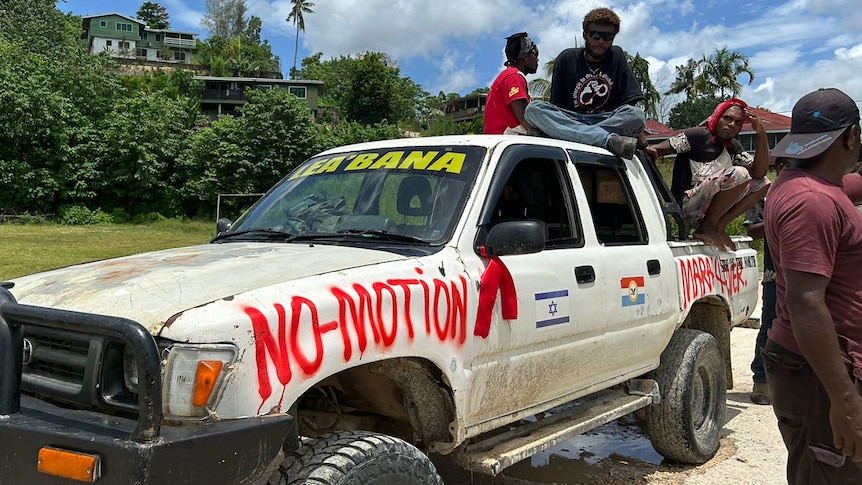 Solomon Islanders sit on a white truck that is spray painted with the words no-motion