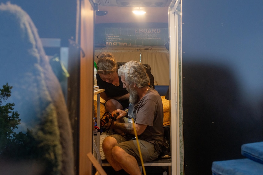 A man and a woman work on the interior of a van by dim incandescent light.