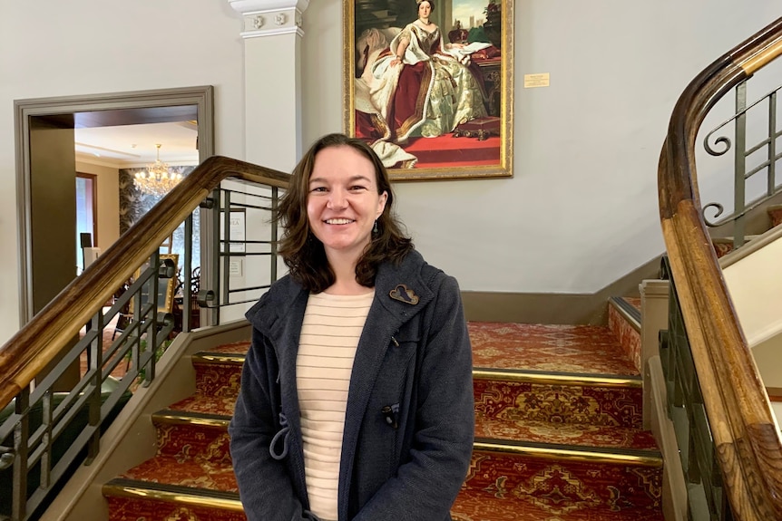 a woman is standing on an old staircase that has red carpet, she's smiling at the camera