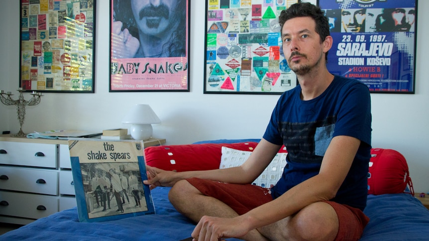 Photographic portrait of Luke Escombe sitting on bed looking at albums produced by The Shake Spears