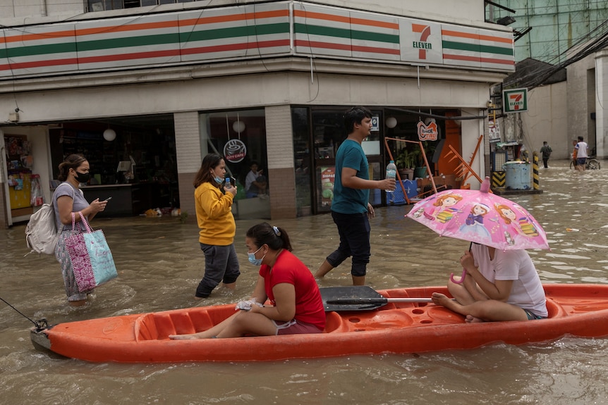 Two woman share a canoe in a flooded street. with a 7/11 store behind them. 