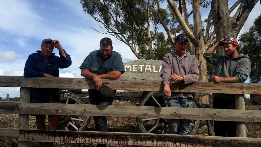 Four farmers standing behind a post and rail fence.