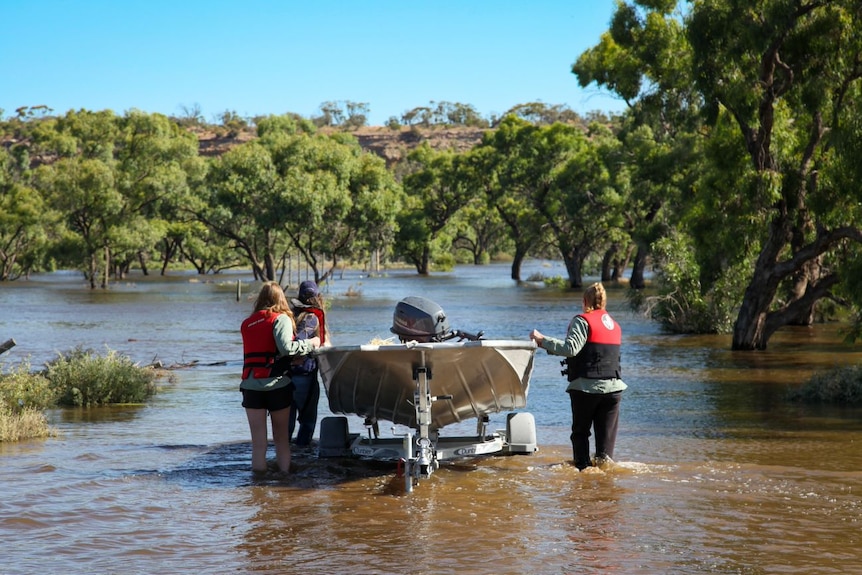 A boat being launched by three rescuers off the riverbank 