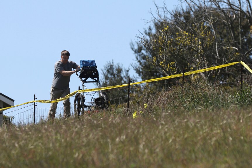 An man uses radar to search the backyard of the home of Ruben Flores with police tape near him